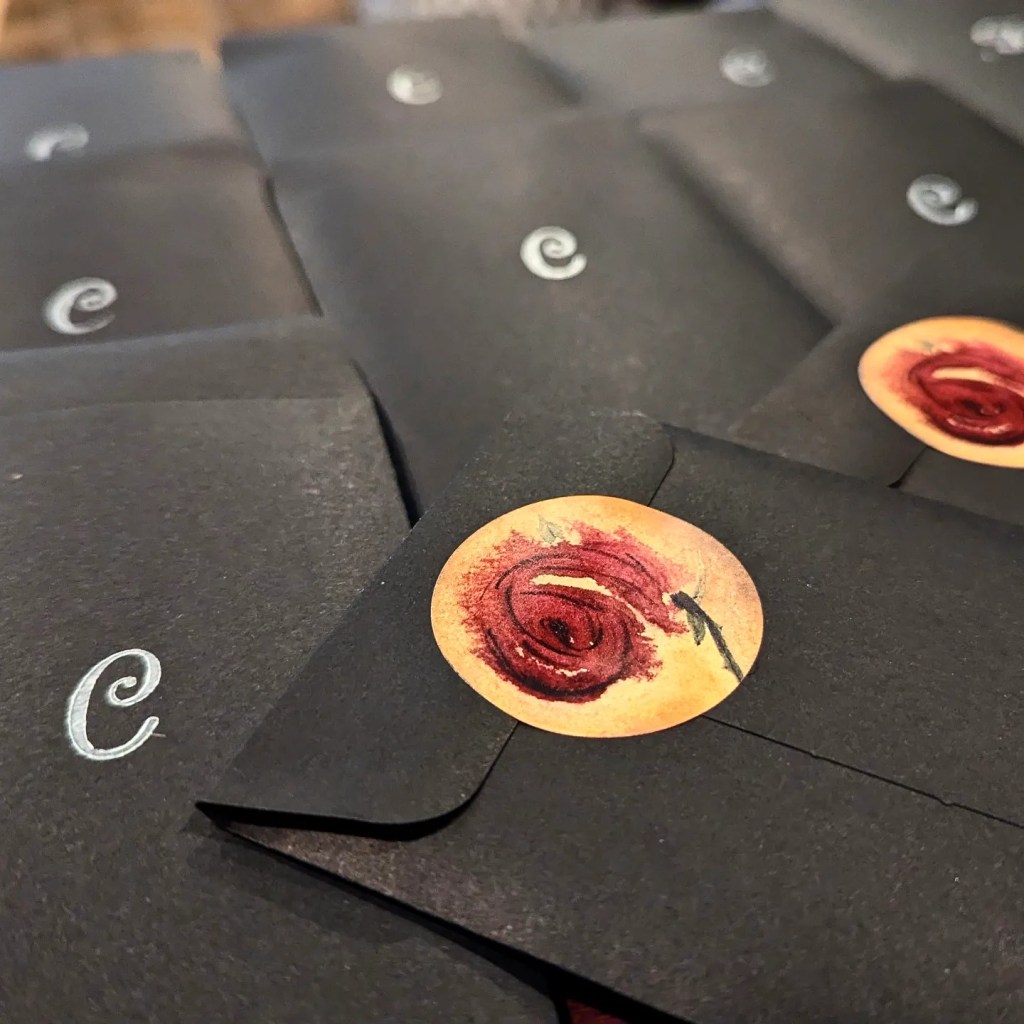 Black paper envelopes big enough for individual Tarot cards, blazoned with an embossed silver letter C and sealed with stickers featuring a watercolor rose.